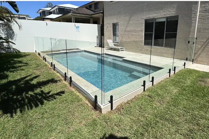 Frameless glass pool fencing surrounding a rectangular backyard swimming pool — Muller's Fencing Sydney