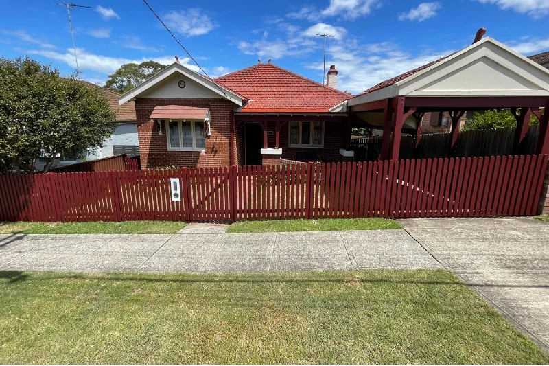 Red painted timber picket fence installed around the front of a residential property — Muller's Fencing Sydney